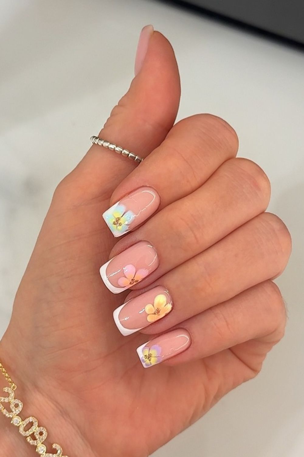 Delicate floral French tip nails perfect for Summer 2025. Features a pink base, white tips, and small colorful flowers.