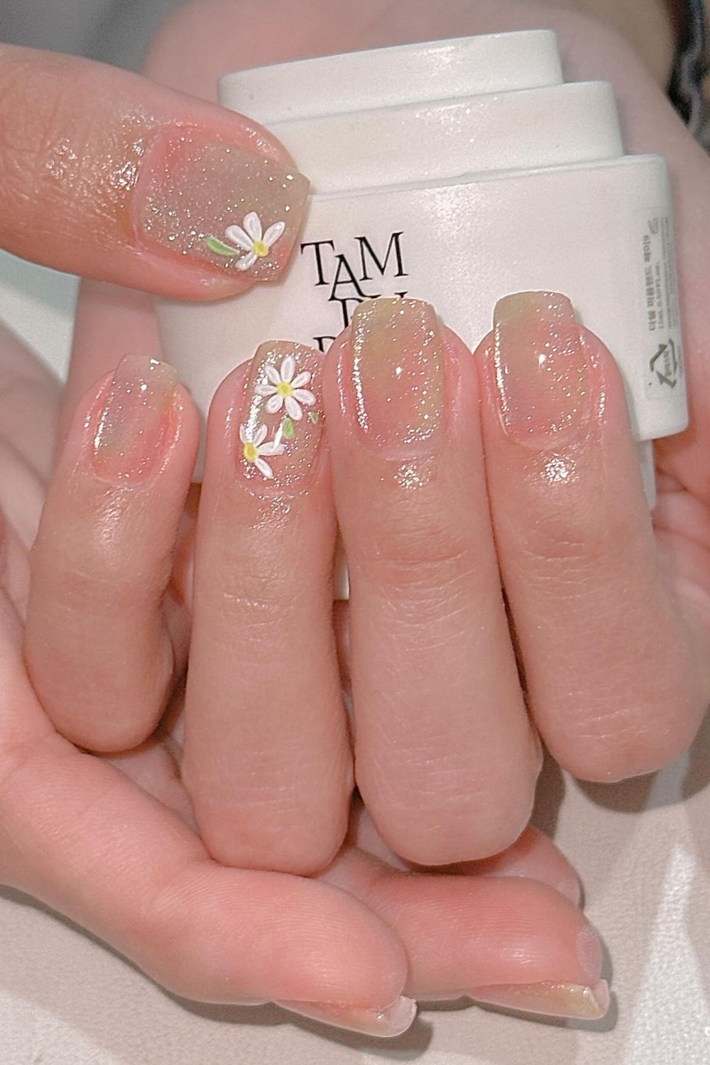 Summer 2025 nude glitter nails with white daisy flower design. Perfect short nail art idea for any skin tone.