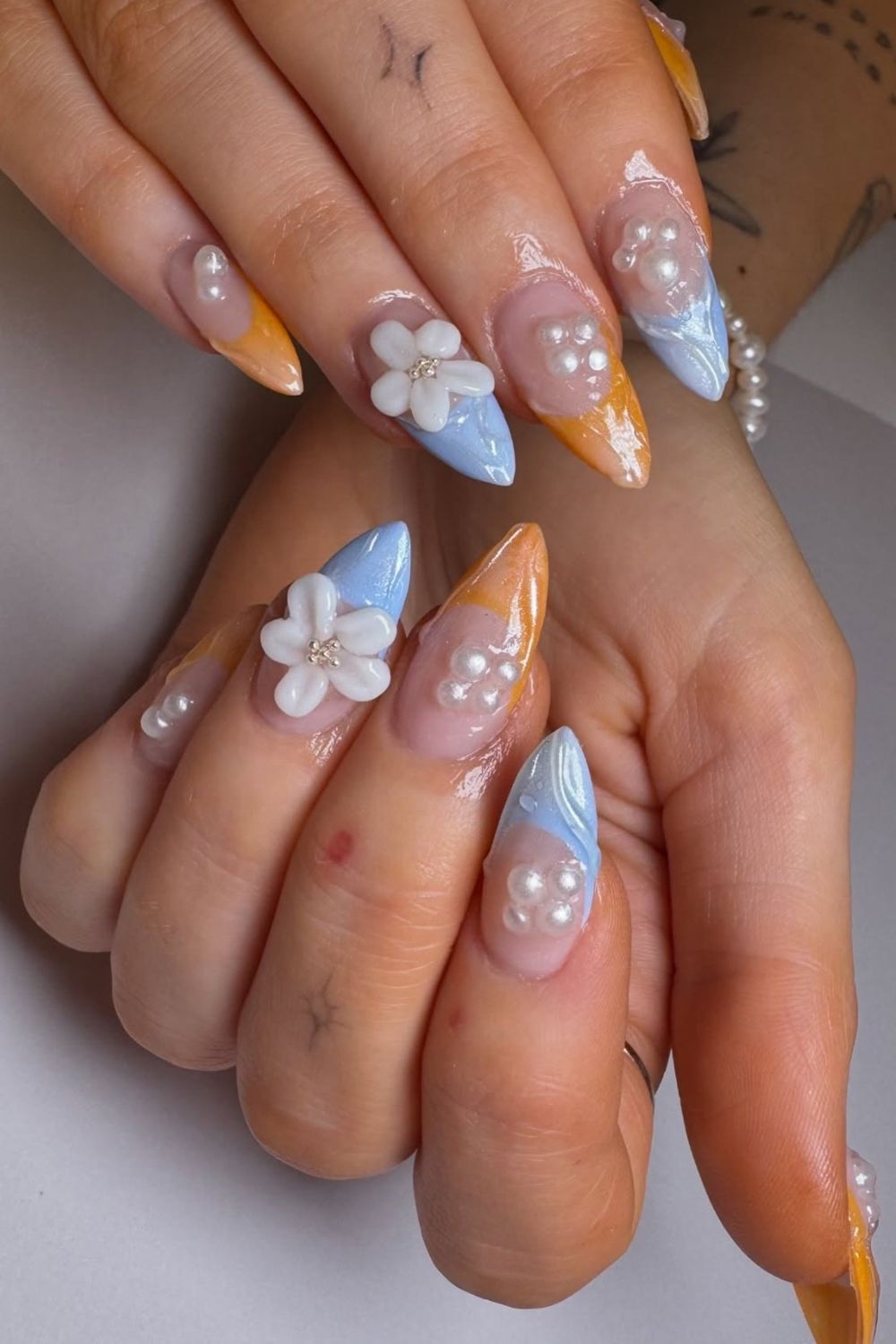 Searching for the best Summer Nails 2025? Discover these unique orange and blue nail ideas with pearls and flowers!
