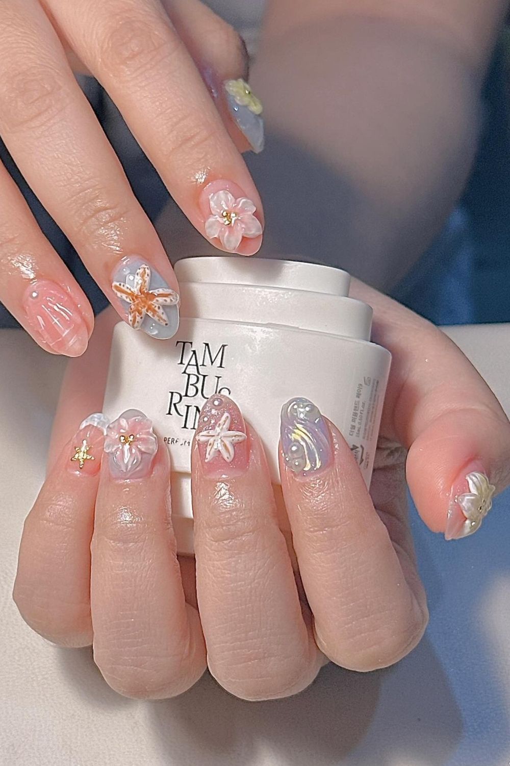 Summer nails 2025 with 3D starfish, flowers, pearls, and gold accents in soft colors.